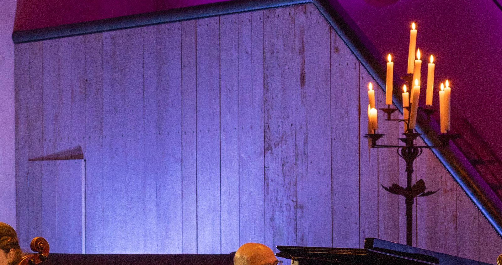 Close-up of the showroom wall: violet light rising up the wooden panels from below, and lit candles on a candelabra in the top right corner.
